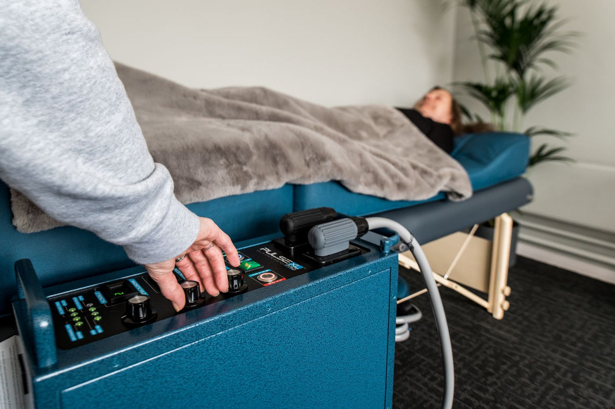 Person adjusting controls on a blue PEMF device in a therapy setting.